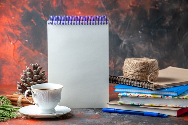 Vooraanzicht van kantoorbenodigdheden en pen kaneel limoenen conifer kegel en een kopje thee op bruine handdoek op donkere achtergrond