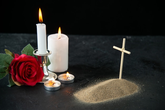 Vooraanzicht van klein graf met rode roos en kaarsen op zwart