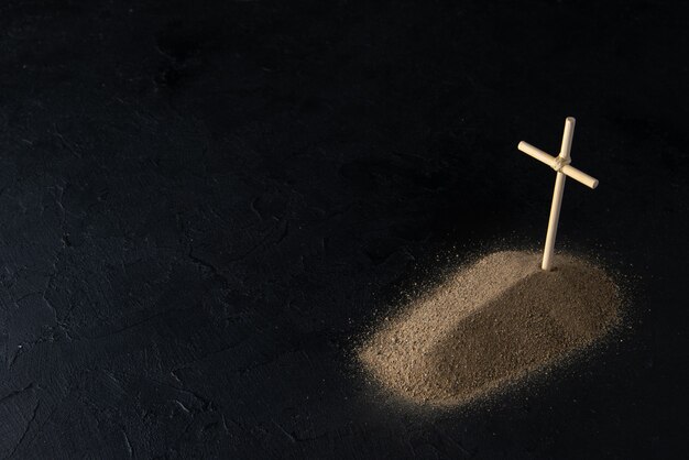 Vooraanzicht van klein graf van zand met stokkruis op zwart