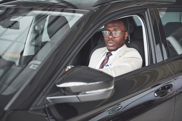 Vooraanzicht van knappe afrikaanse elegante ernstige zakenman bestuurt een auto. Gratis Foto