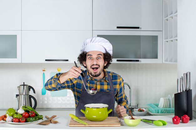 Vooraanzicht van lachende chef-kok met verse groenten die kant-en-klaarmaaltijden proeven in de witte keuken