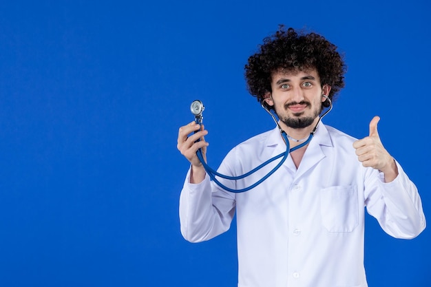 Vooraanzicht van lachende mannelijke arts in medisch pak met stethoscoop op blauwe achtergrond vaccin pandemie covid virus gezondheid ziekenhuis drug Gratis Foto