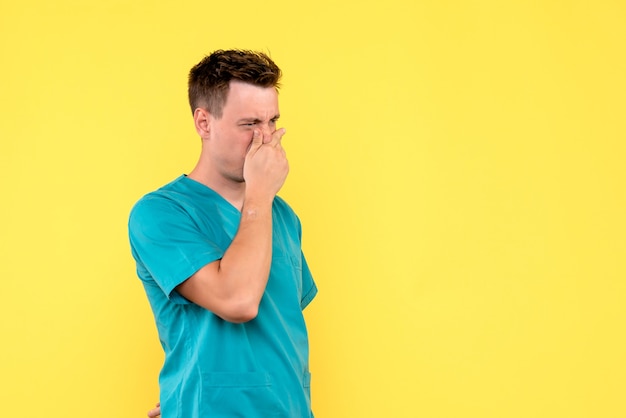 Vooraanzicht van mannelijke arts die zijn neus op gele muur behandelt