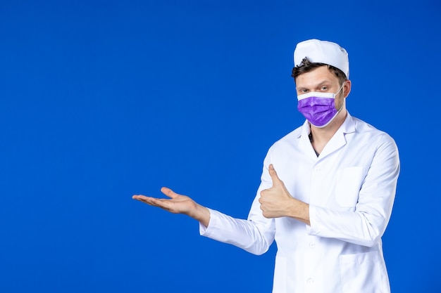 Vooraanzicht van mannelijke arts in medisch kostuum en paars masker op blauw