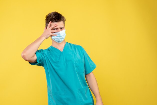 Vooraanzicht van mannelijke arts in medisch kostuum en steriel masker op gele muur