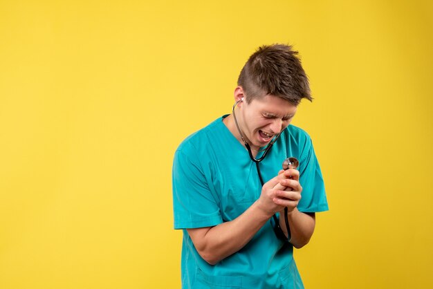 Vooraanzicht van mannelijke arts in medisch kostuum met stethoscoop op gele muur