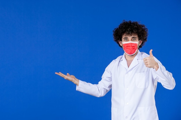Vooraanzicht van mannelijke arts in medisch pak en masker op blauwe achtergrond vaccin ziekenhuis covid- virus pandemie coronavirus geneeskunde medicijnen gezondheid