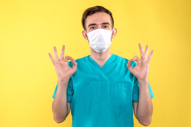 Vooraanzicht van mannelijke arts in steriel masker op gele muur