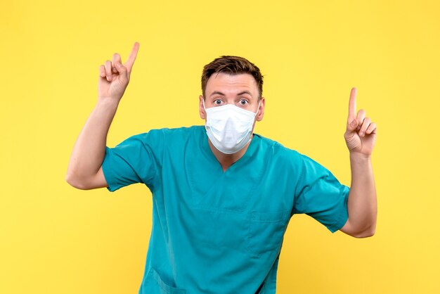 Vooraanzicht van mannelijke arts in steriel masker op gele muur