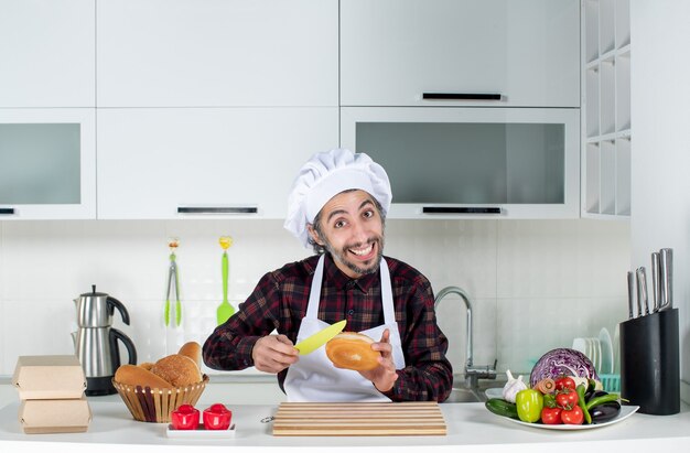 Vooraanzicht van mannelijke chef-kok die brood met geel mes in de keuken snijdt