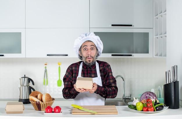 Vooraanzicht van mannelijke chef-kok in uniforme holdingsdoos in moderne keuken