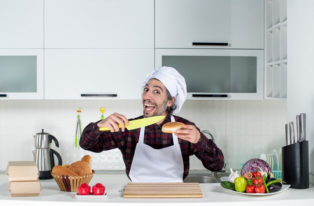 Vooraanzicht van mannelijke chef-kok met brood en geel mes in de keuken