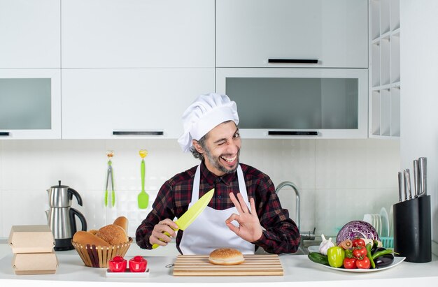 Vooraanzicht van mannelijke chef-kok met geel mes maken okey teken in de keuken
