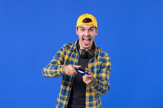 Vooraanzicht van mannelijke gamer met gamepad die videogame speelt op blauwe muur