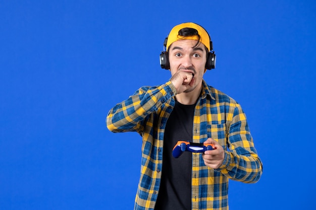 Vooraanzicht van mannelijke gamer met gamepad en koptelefoon die videogame speelt op blauwe muur