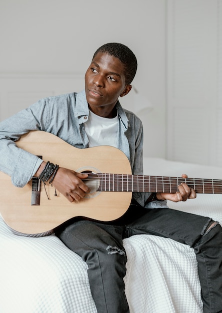 Vooraanzicht van mannelijke muzikant met gitaar op bed