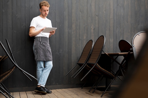 Vooraanzicht van mannelijke ober met schort en tablet