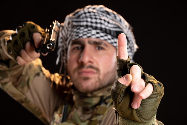 Vooraanzicht van mannelijke soldaat in camouflage die een pistool op de zwarte muur richt