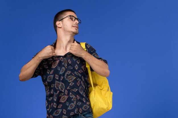 Vooraanzicht van mannelijke student in donker katoenen overhemd met gele rugzak op de blauwe muur