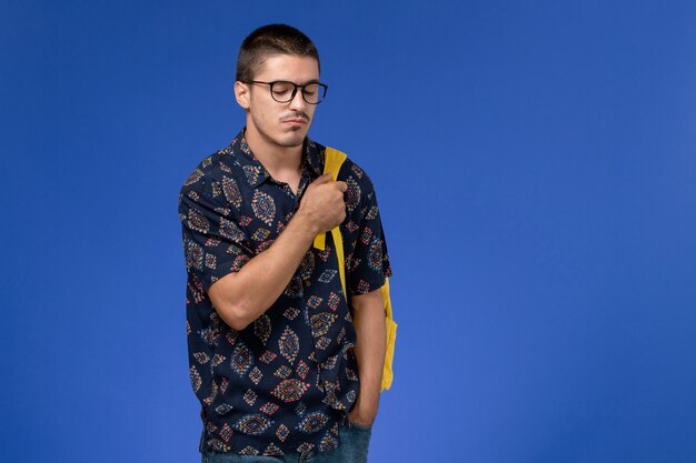 Vooraanzicht van mannelijke student in donker overhemd die gele rugzak draagt die enkel op lichtblauwe muur staat