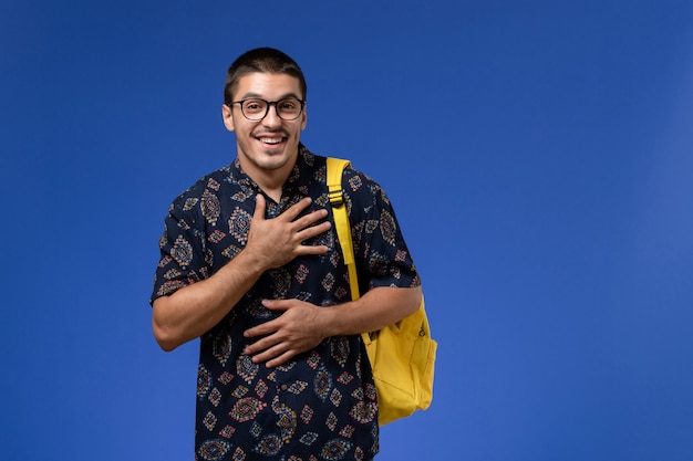 Vooraanzicht van mannelijke student in donker overhemd gele rugzak dragen op de blauwe muur