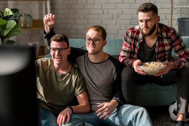 Vooraanzicht van mannelijke vrienden die naar sport op tv kijken en samen snacks hebben