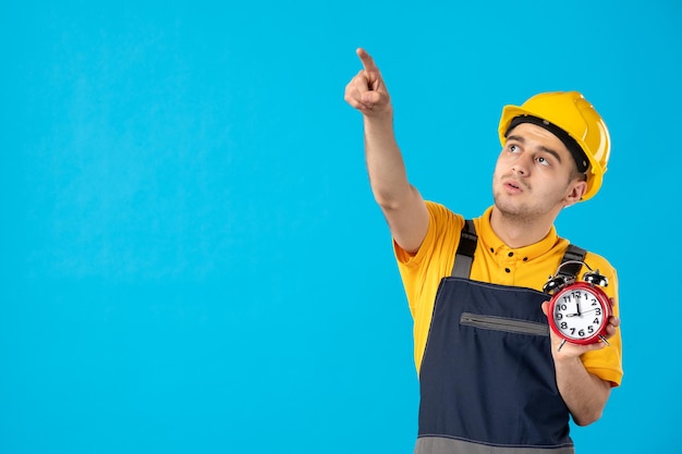 Vooraanzicht van mannelijke werknemer in geel uniform met klokken die op blauw wijzen