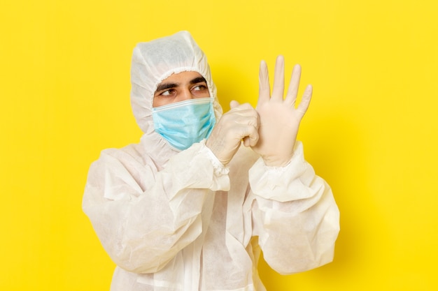 Gratis foto vooraanzicht van mannelijke wetenschappelijke werker in speciaal beschermend pak en met masker die handschoenen op gele muur dragen