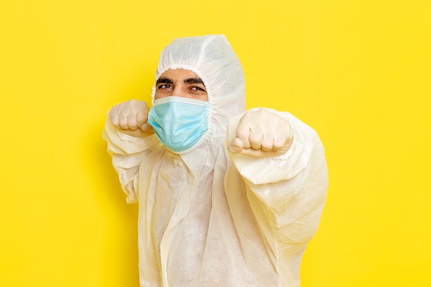 Gratis foto vooraanzicht van mannelijke wetenschappelijke werker in speciaal beschermend pak en met masker op de lichtgele muur