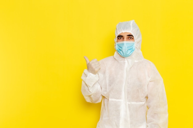 Vooraanzicht van mannelijke wetenschappelijke werker in speciaal beschermend wit pak met masker op de lichtgele muur