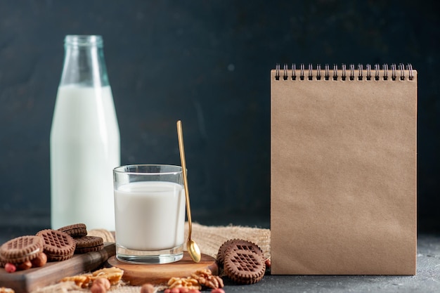 Vooraanzicht van met room gevulde chocoladekoekjes en een glas en fles met melknotenpinda's op bruin handdoeknotitieboekje op zwarte achtergrond