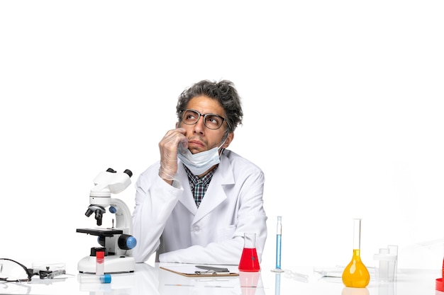 Vooraanzicht van middelbare leeftijd wetenschapper in speciaal wit pak aan tafel zitten met oplossingen