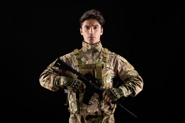 Vooraanzicht van militaire militair in uniform met geweer op zwarte muur