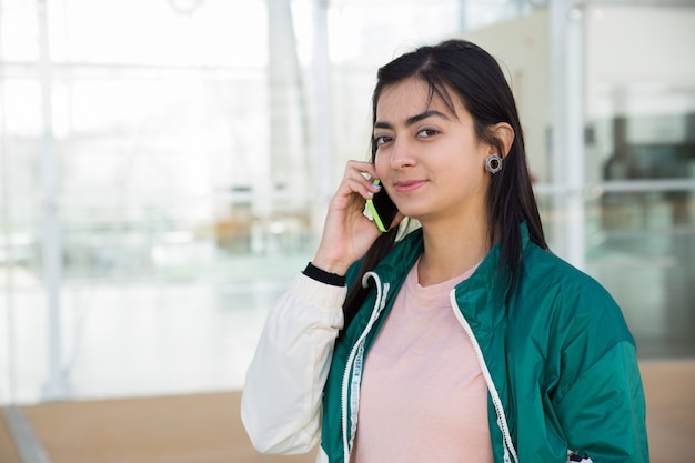 Vooraanzicht van mooie vrouw die op telefoon spreekt, die camera bekijkt