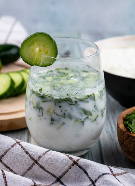 Vooraanzicht van okroshka in een glas met een komkommer en een witte geruite handdoek