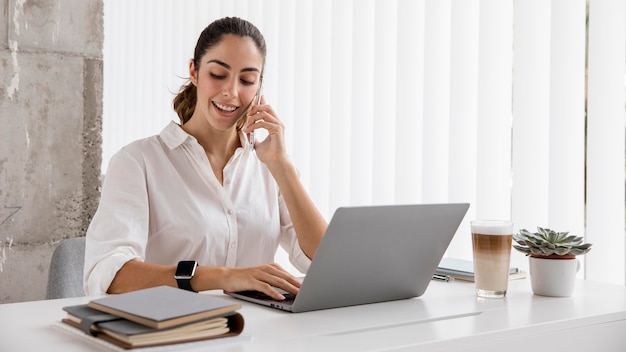 Vooraanzicht van onderneemster die met smartphone en laptop werkt