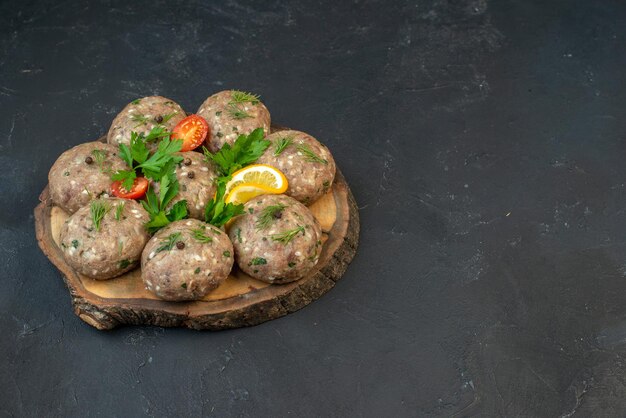 Vooraanzicht van ongekookte gehaktballen op een houten snijplank tomaten met stengels op donkere golfachtergrond met vrije ruimte