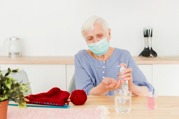 Gratis foto vooraanzicht van oudere vrouw die handdesinfecterend middel gebruikt terwijl het breien