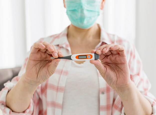 Vooraanzicht van oudere vrouw met medisch masker dat thermometer steunt