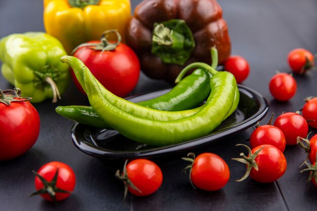 Vooraanzicht van plaat van peper met tomaten en andere paprika's rond op zwarte ondergrond