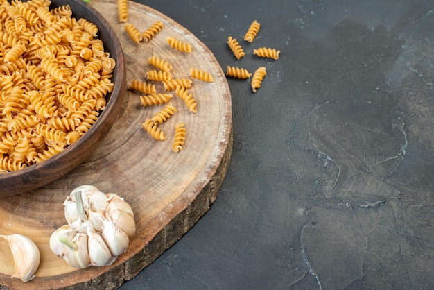 Vooraanzicht van rauwe pasta's binnen en buiten bruine pot knoflook aan de rechterkant op donkerblauwe kleur achtergrond
