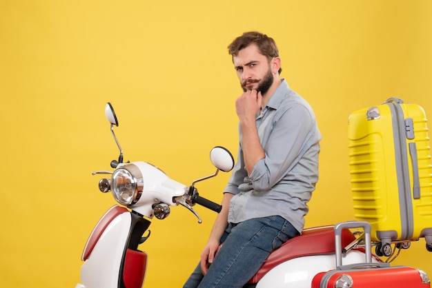 Vooraanzicht van reisconcept met doordachte jongeman zittend op moto met koffers erop op geel