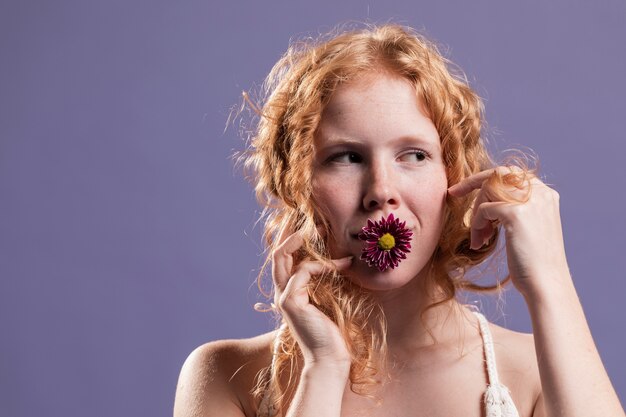 Vooraanzicht van roodharigevrouw het stellen met een chrysant op haar mond en exemplaarruimte