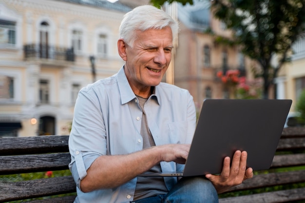Vooraanzicht van senior man buiten op bankje met laptop