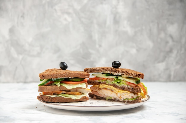 Vooraanzicht van smakelijke sandwich met zwart brood versierd met olijf op een bord op een gekleurd wit oppervlak