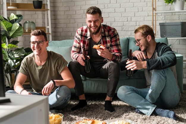 Vooraanzicht van smiley mannelijke vrienden met pizza en sport kijken op tv met bier