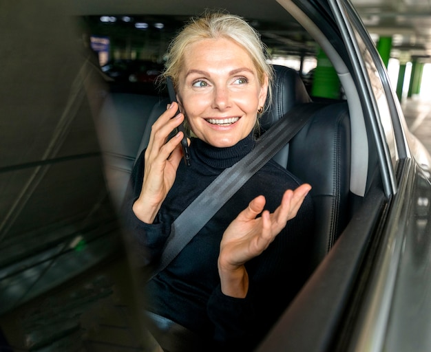 Vooraanzicht van smiley oudere zakenvrouw praten aan de telefoon in auto