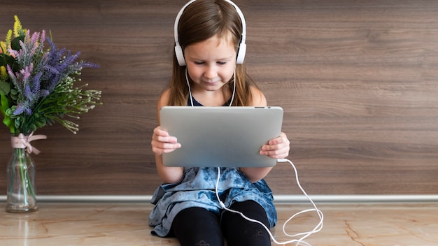 Gratis foto vooraanzicht van smileymeisje dat tablet met hoofdtelefoons gebruikt