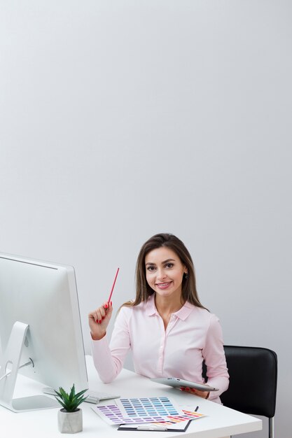 Vooraanzicht van smileyvrouw die bij bureau werkt en tablet houdt