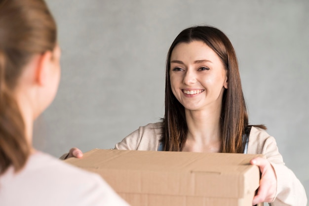 Gratis foto vooraanzicht van smileyvrouw die kartondoos overhandigt aan klant